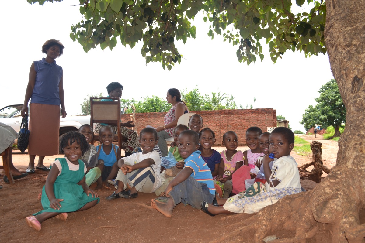 Group of smiling children sitting under a mango tree
